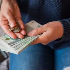 Dłonie liczą banknoty i monety. Widać stos banknotów 100 zł, które mogą stanowić część pensji 10000 brutto.