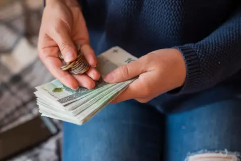 Dłonie liczą banknoty i monety. Widać stos banknotów 100 zł, które mogą stanowić część pensji 10000 brutto.