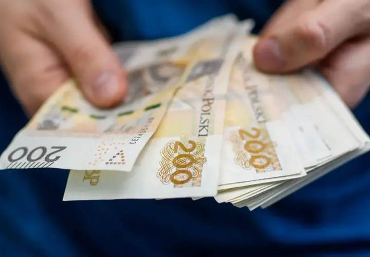 Dłonie trzymają plik banknotów 200 zł. Zastanawiasz się, ile wynosi zasiłek dla bezrobotnych?