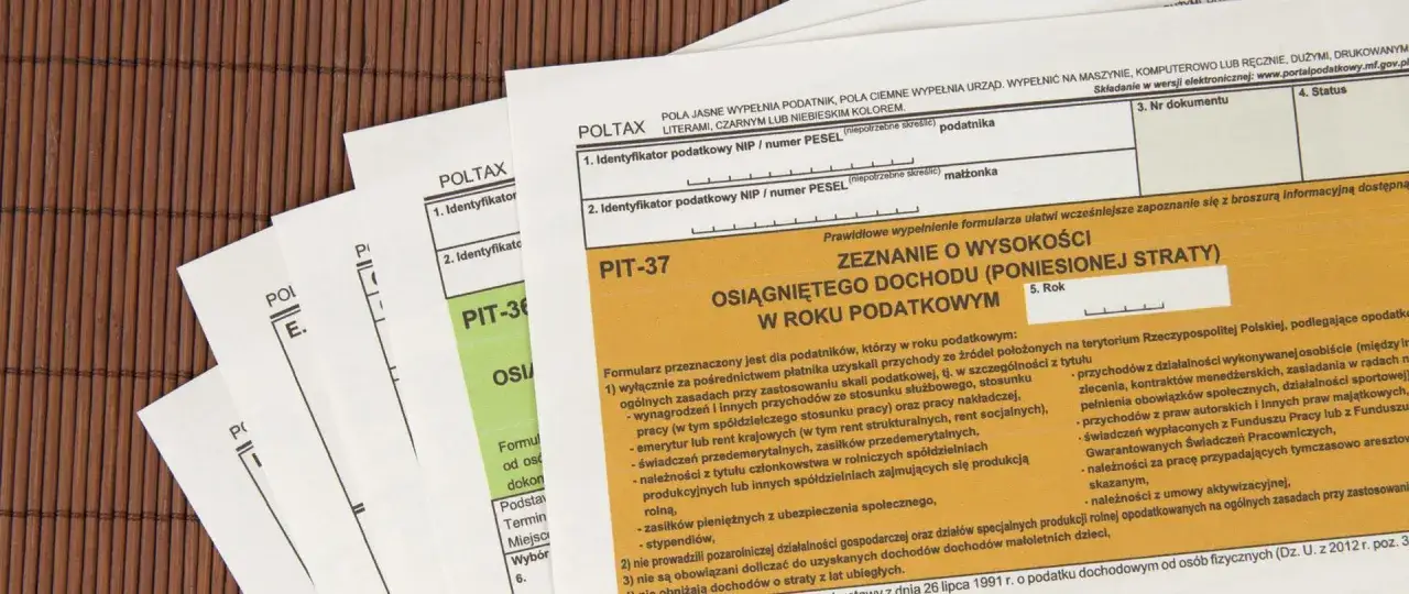 Formularze PIT-37, PIT-36 i inne dokumenty podatkowe na brązowym tle. PIT-37 to zeznanie o wysokości osiągniętego dochodu.