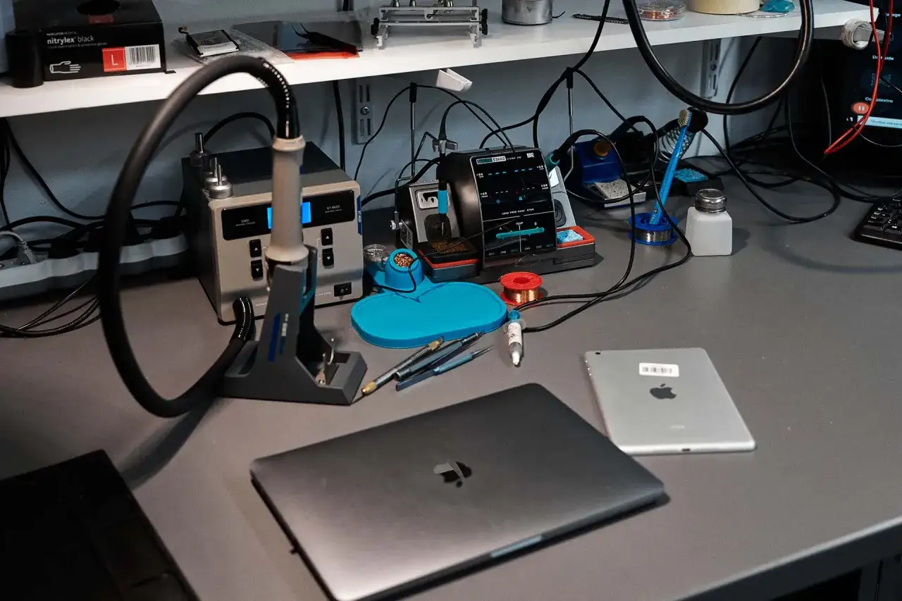 Serwisant przygotowuje się do pracy przy laptopie i tablecie. Na stole lutownica, narzędzia i cyna.